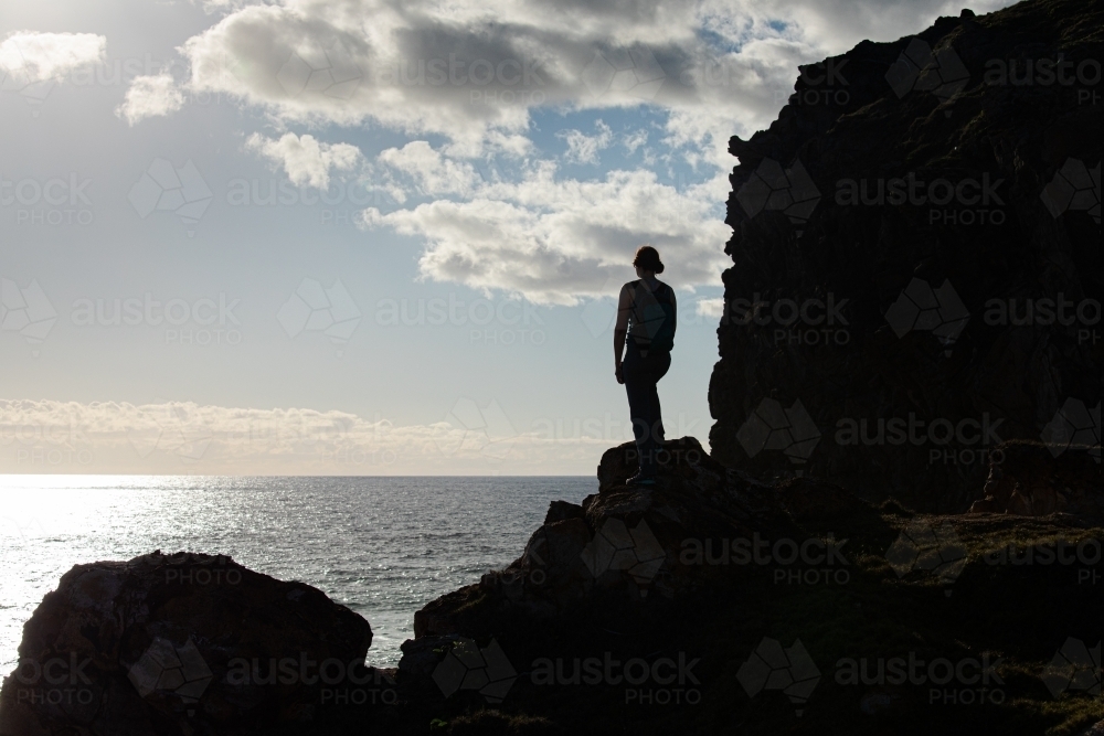 Woman standing on dark rocky outline by the sea - Australian Stock Image