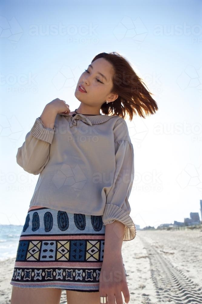 Woman standing on the beach with the sun behind her and the wind in her hair - Australian Stock Image