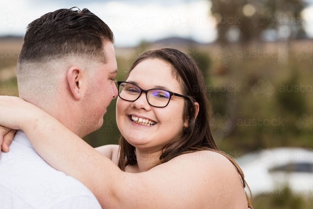 Woman standing with arms around boyfriends neck smiling - Australian Stock Image