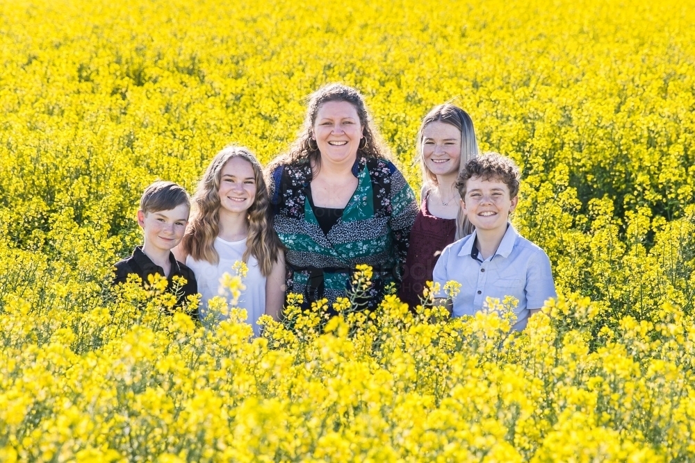 Woman standing with four children family in canola paddock on farm - Australian Stock Image
