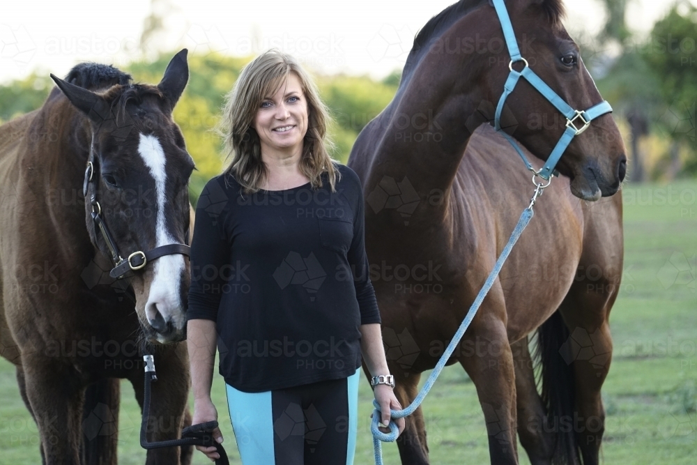 Woman standing with horses in paddock - Australian Stock Image
