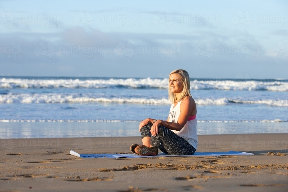 woman stretching on a mat at the beach - Australian Stock Image