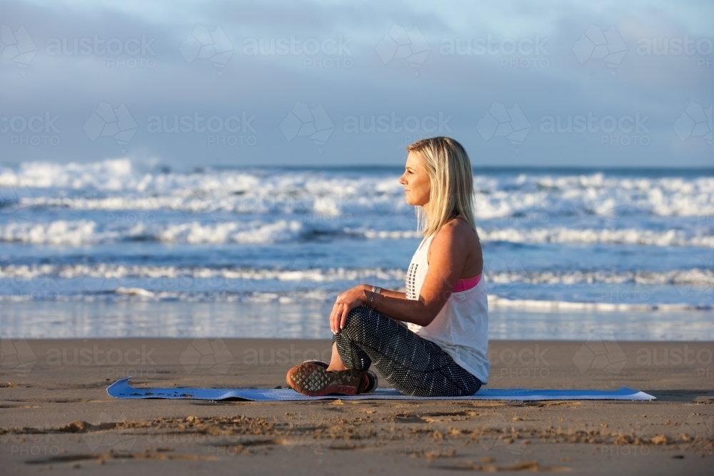 Woman stretching on a mat at the beach - Australian Stock Image