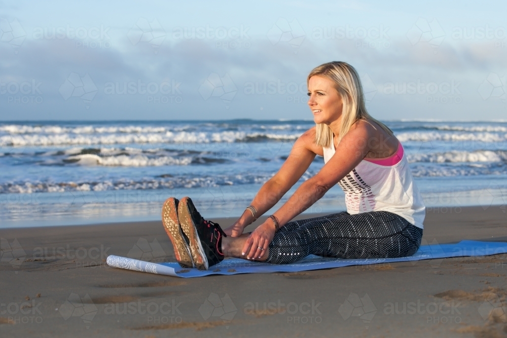woman stretching on a mat at the beach - Australian Stock Image