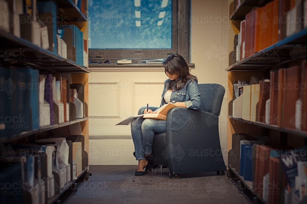 Woman studying on a chair in a library near book shelves - Australian Stock Image