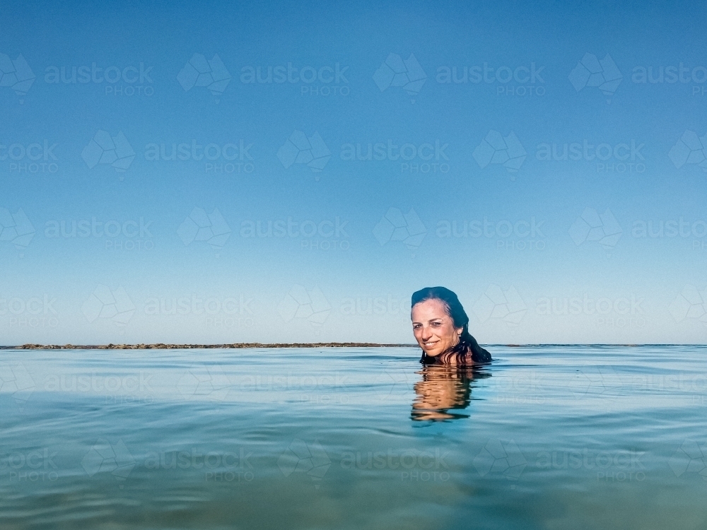 Woman submerged and floating in calm ocean on clear day - Australian Stock Image