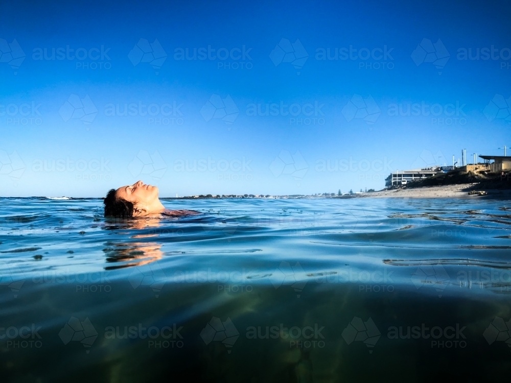 Woman submerged and floating in calm ocean on clear day - Australian Stock Image