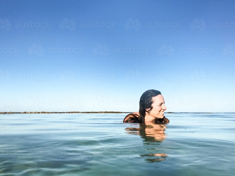 Woman submerged and floating in calm ocean on clear day - Australian Stock Image