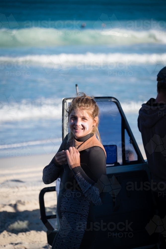 Woman suiting up for a surf next to 4WD on beach - Australian Stock Image