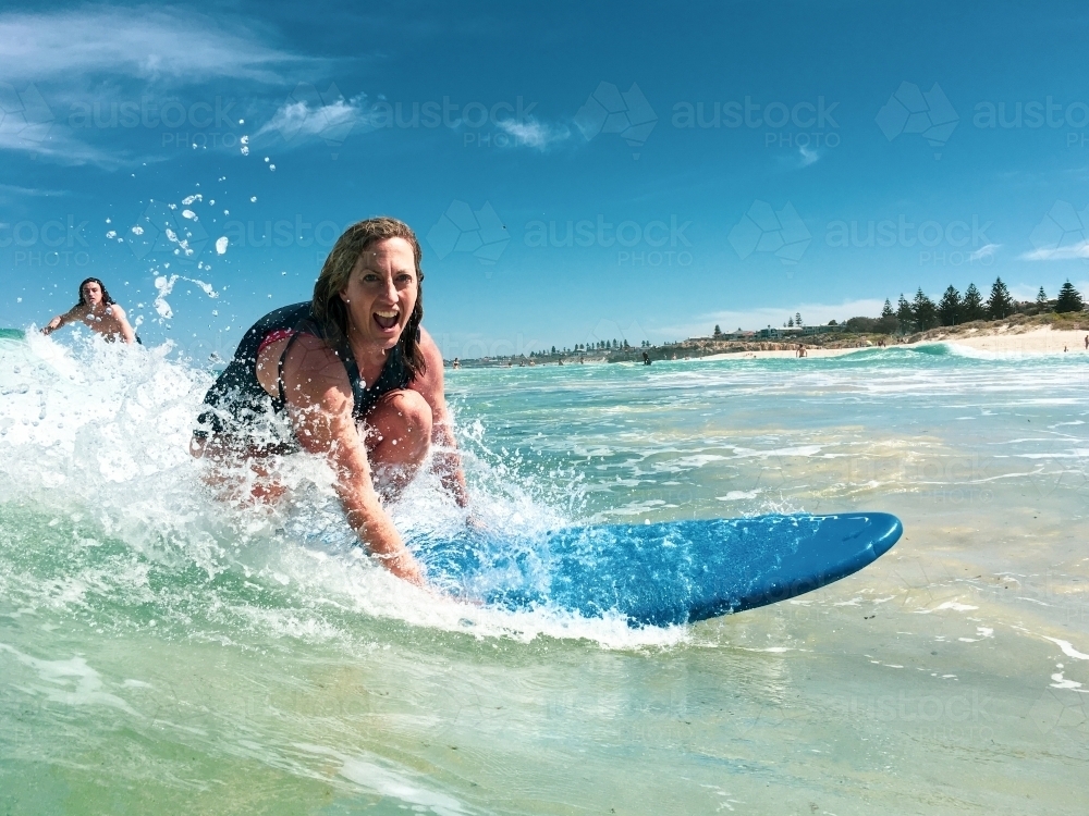 Woman surfing wave on soft board surfboard laughing - Australian Stock Image