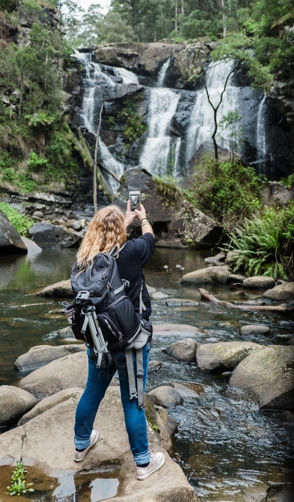 Woman taking a phone photo at the waterfall. - Australian Stock Image