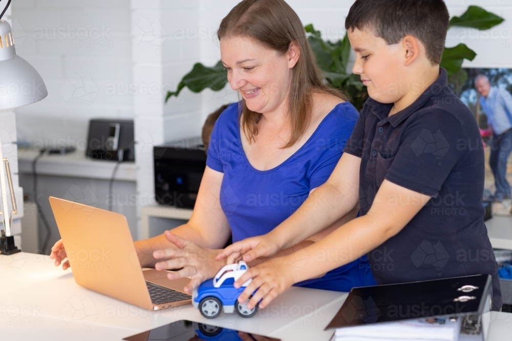 woman trying to work on computer while child plays with car on her desk - Australian Stock Image