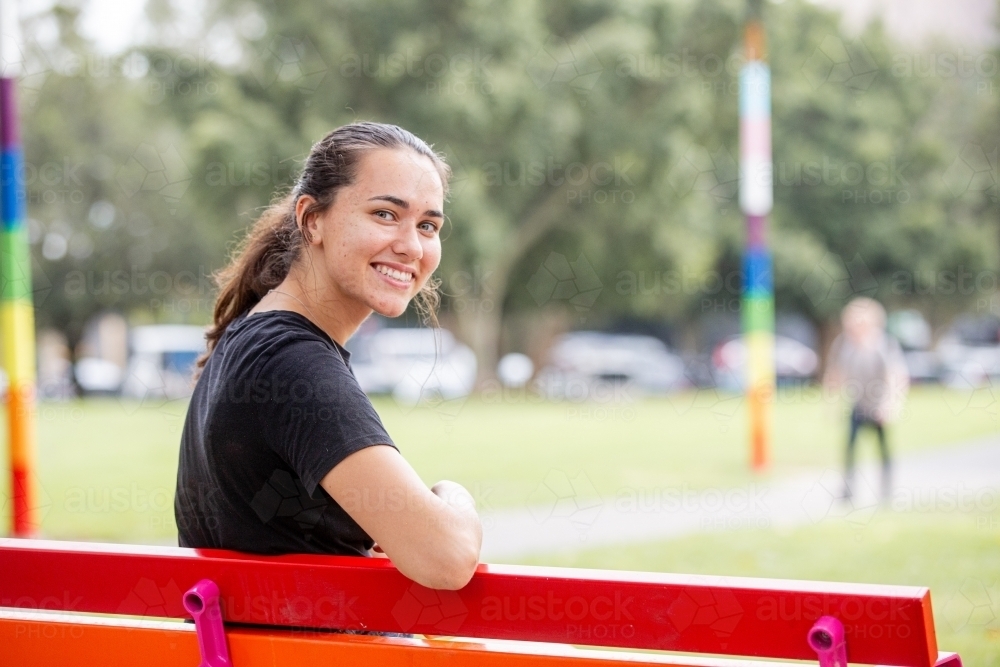 Woman turning to smile with her elbow resting on a park bench - Australian Stock Image