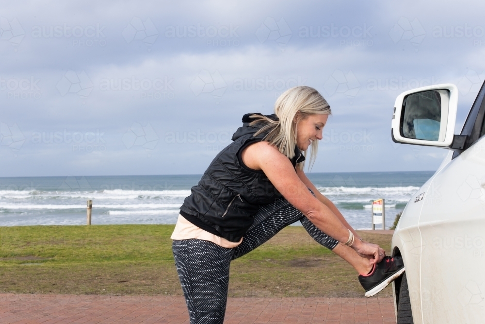 woman tying her shoelace on a car wheel - Australian Stock Image
