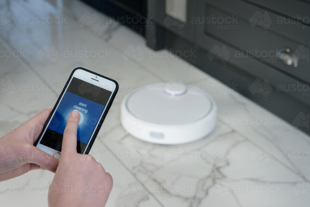 woman using a photo to control a robotic vacuum cleaner - Australian Stock Image