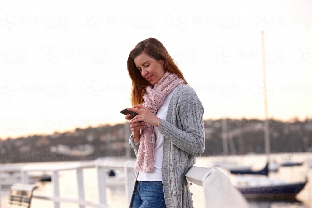 Woman using mobile phone on wharf during winter - Australian Stock Image