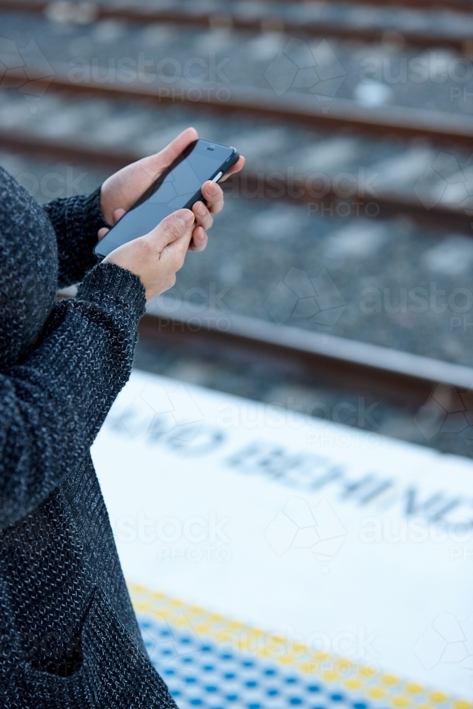 Woman waiting at train station holding mobile phone - Australian Stock Image