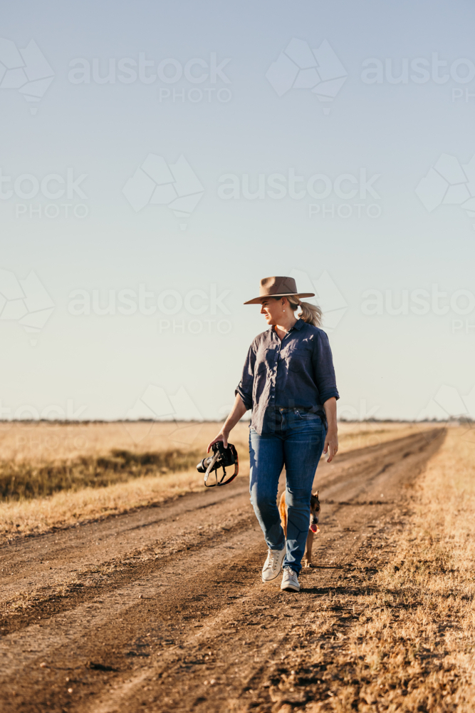 Woman walking along road facing camera in rural farm setting - Australian Stock Image