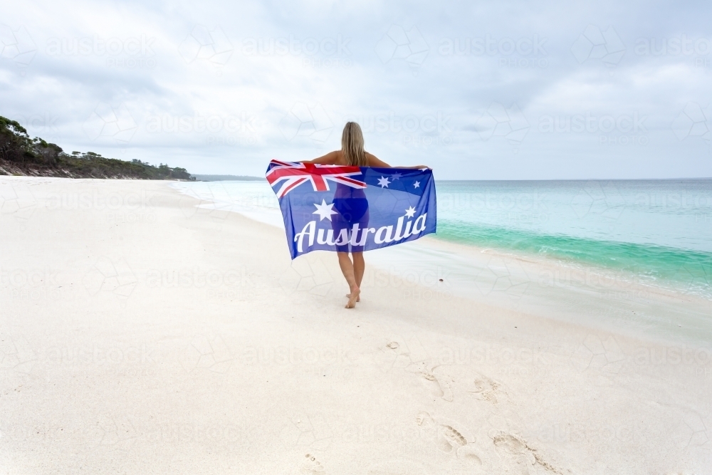 Woman walking along the beach holding Australian Flag - Australian Stock Image