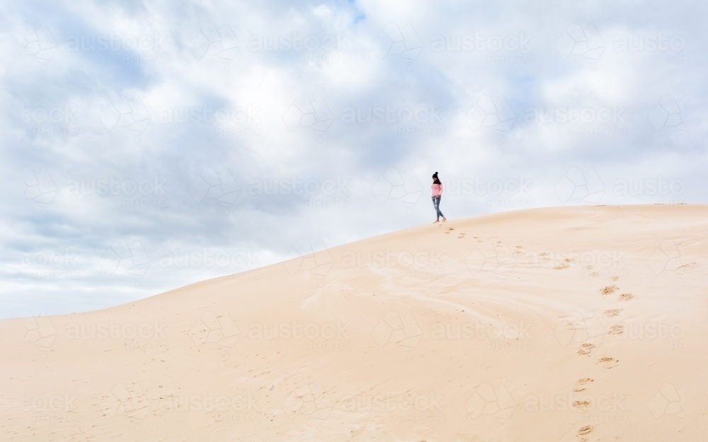 Woman walking away over sand dune - Australian Stock Image
