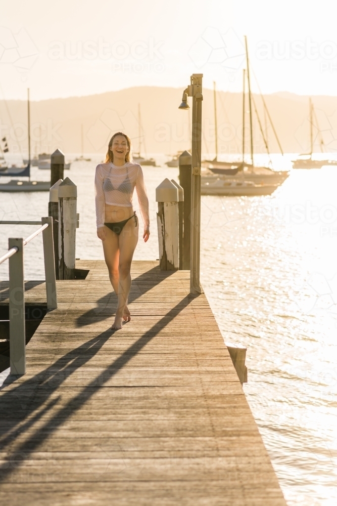 woman walking down jetty at sunset - Australian Stock Image
