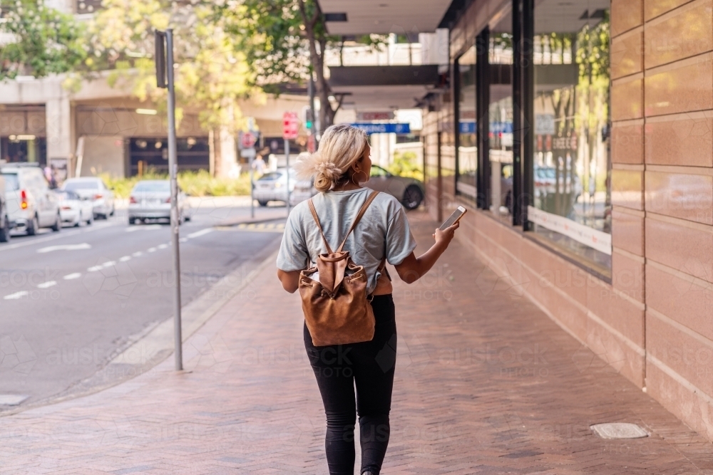 woman walking in the city, looking at phone - Australian Stock Image