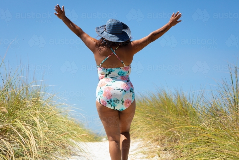 woman walking on dune path with arms raised in exultation - Australian Stock Image