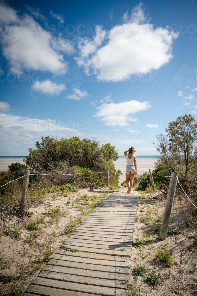 woman walking on slat wood beach path with beach in background - Australian Stock Image