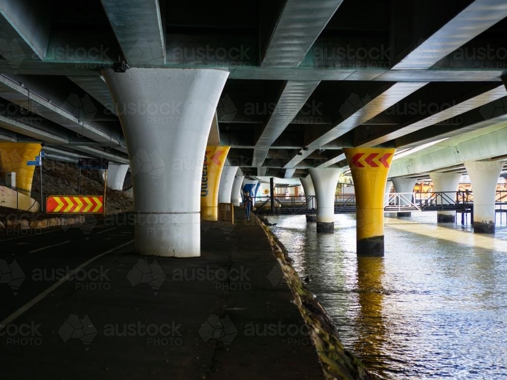 Woman walking on the banks of a river under an expressway - Australian Stock Image