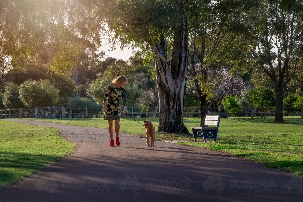 Woman walking with dog on footpath in a park - Australian Stock Image