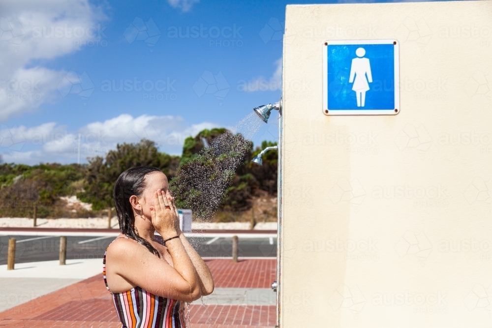 Woman washing off at beach shower after swimming in the sea - Australian Stock Image