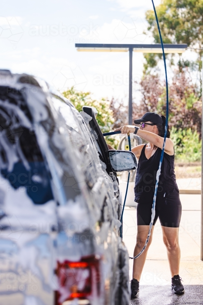 Woman washing vehicle in self-service car wash bay - Australian Stock Image