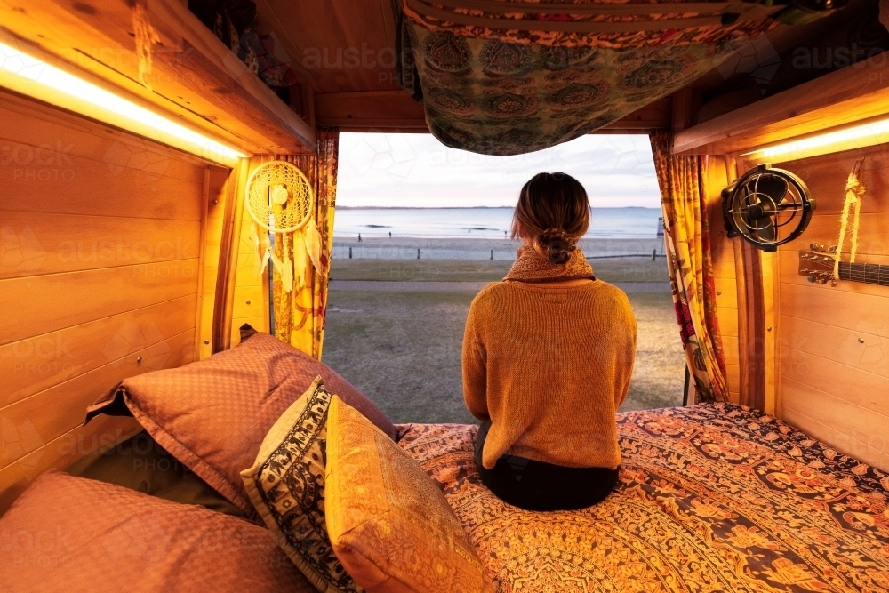 Woman watching sunset over beach from bohemian camper van in a van life theme - Australian Stock Image