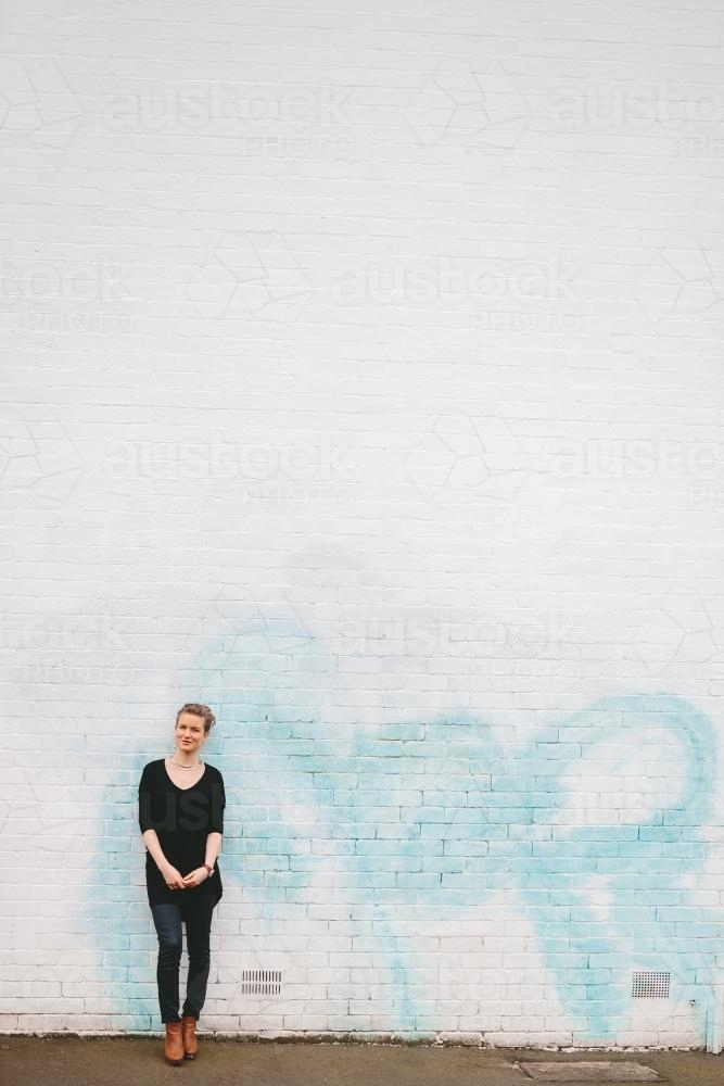 Woman wearing black against white brick wall - Australian Stock Image