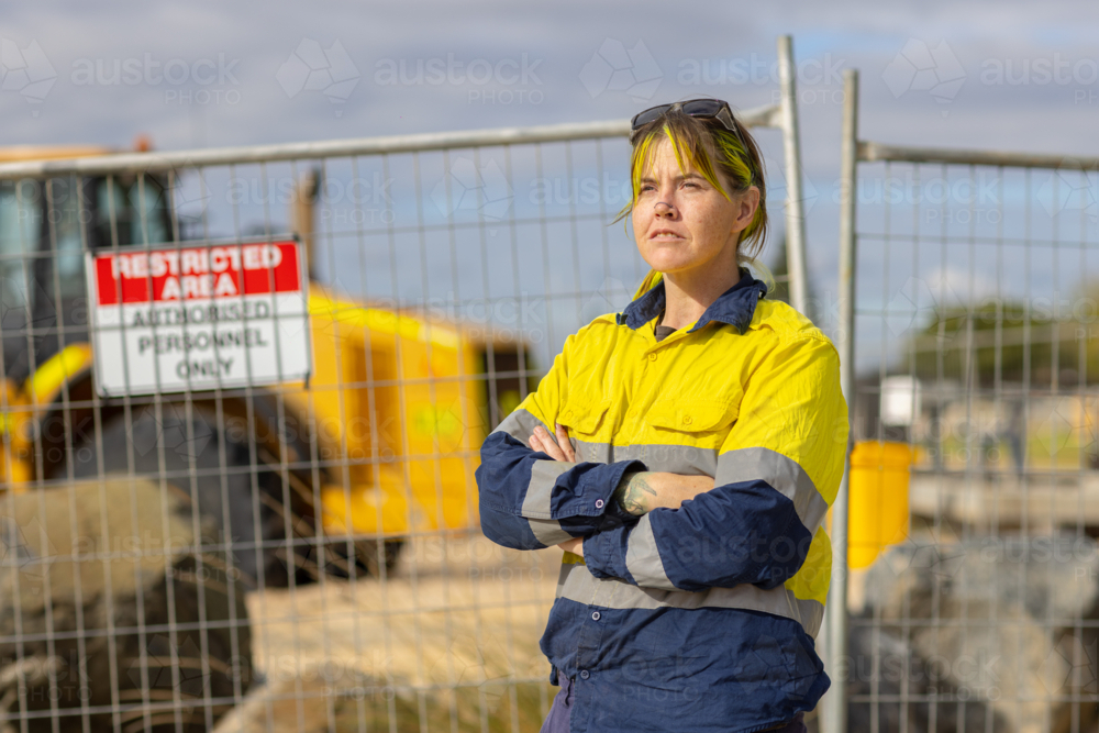 woman wearing hi-vis workwear standing with arms crossed in front of restricted area - Australian Stock Image