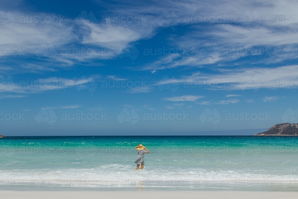 Woman wearing straw hat wading into the blue ocean - Australian Stock Image