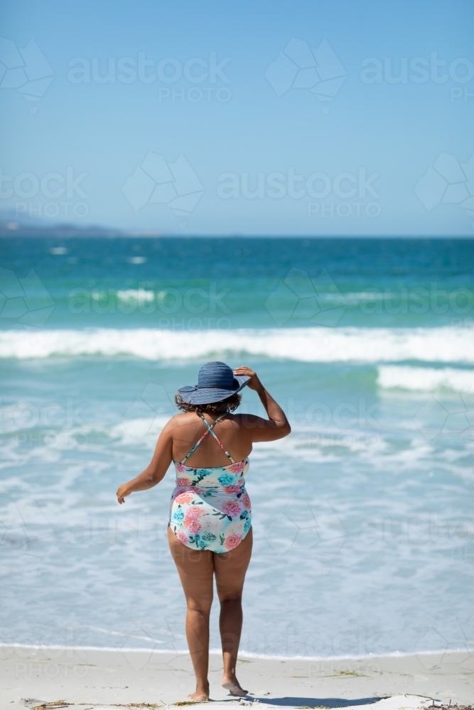 woman wearing sunhat and swimsuit on beach seen from behind - Australian Stock Image