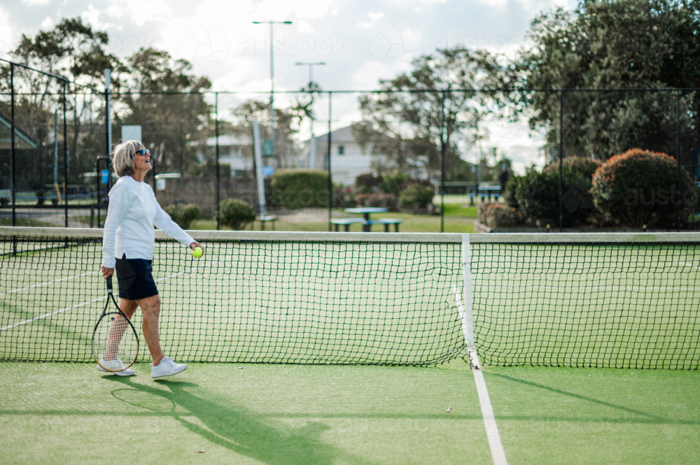 Woman wearing tennis attire walks across the court while holding a tennis ball - Australian Stock Image