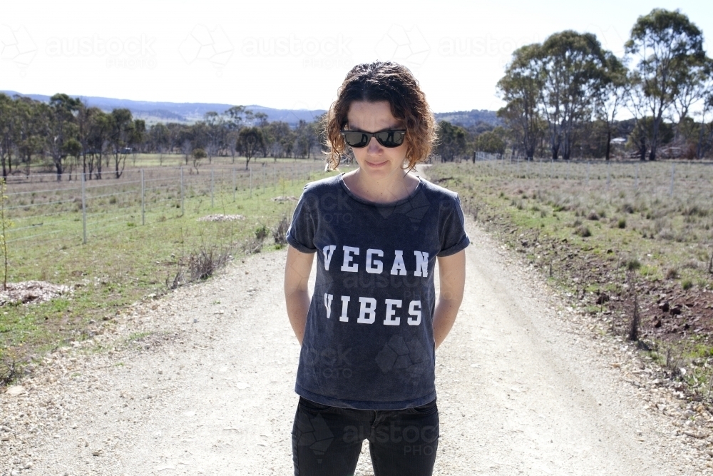Woman wearing vegan slogan t-shirt standing on rural dirt road - Australian Stock Image