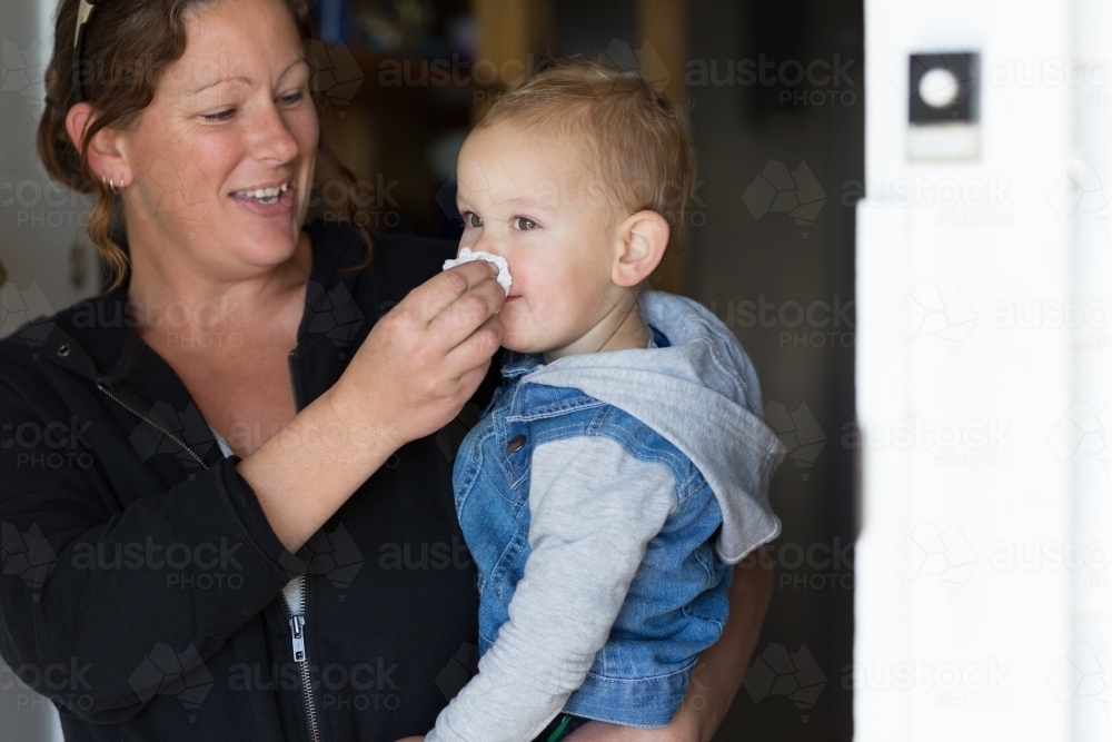 Woman wiping child's nose with a tissue - Australian Stock Image