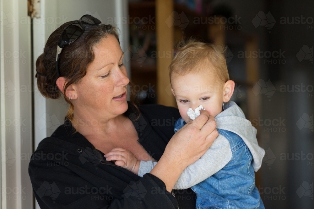 Woman wiping little kid's nose with tissue - Australian Stock Image