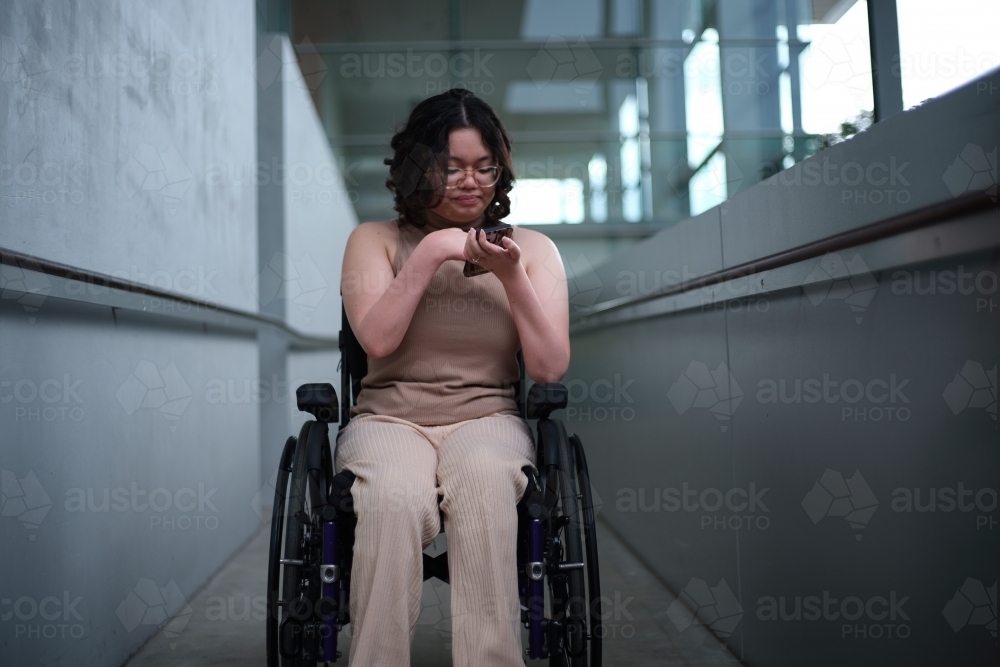 woman with a disability sitting in a wheelchair looking down at her mobile phone - Australian Stock Image