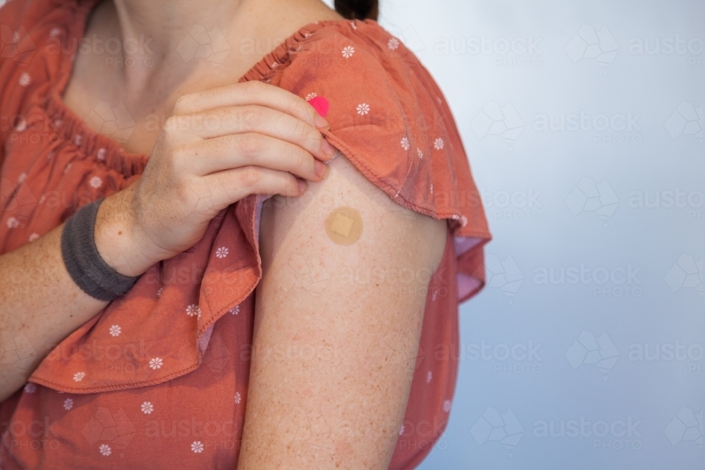 Woman with band aid over Covid-19 vaccine injection site - Australian Stock Image