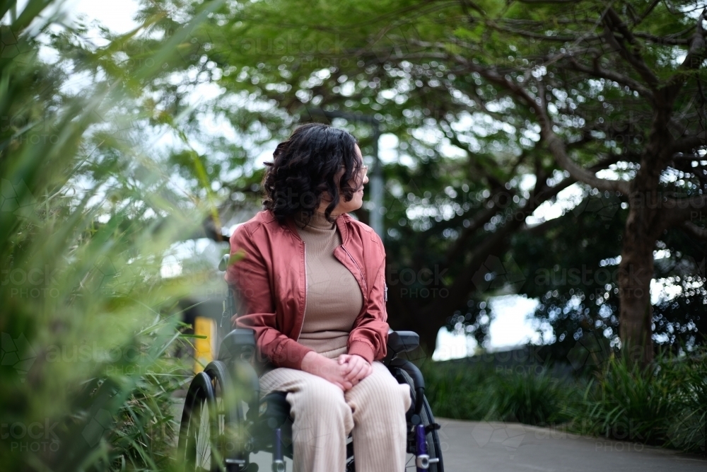 Woman with disability sitting in a wheelchair outside next to a tall grass - Australian Stock Image