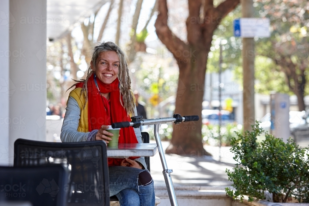 Woman with dreadlocks and scooter at a cafe in the city - Australian Stock Image