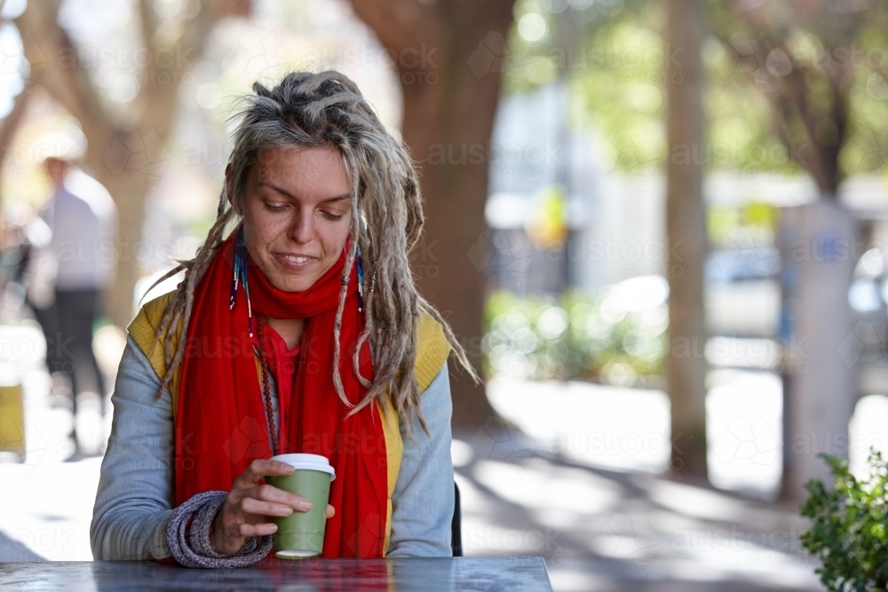 Woman with dreadlocks drinking coffee outdoors at cafe - Australian Stock Image