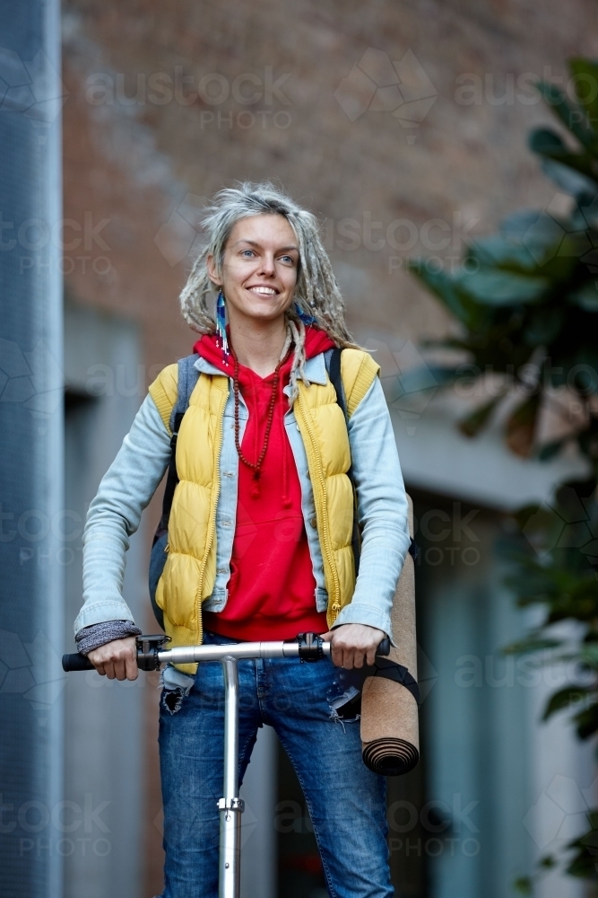 Woman with dreadlocks on electric scooter going to her yoga class - Australian Stock Image