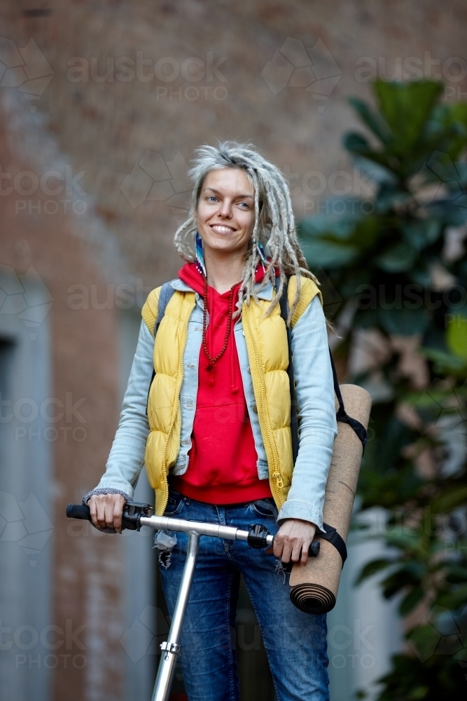 Woman with dreadlocks on electric scooter going to yoga class - Australian Stock Image