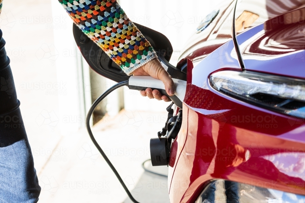 Image of Woman with electric vehicle charging plug plugging it into car