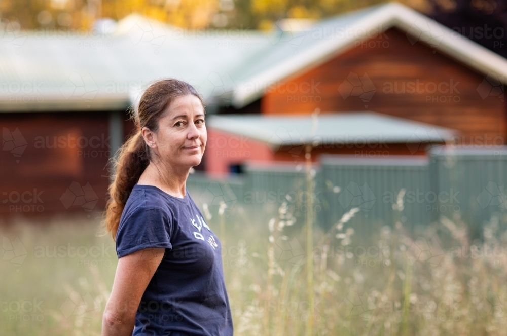 woman with hands behind her back outside country house - Australian Stock Image